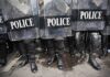 Police officers in riot gear standing behind shields marked POLICE