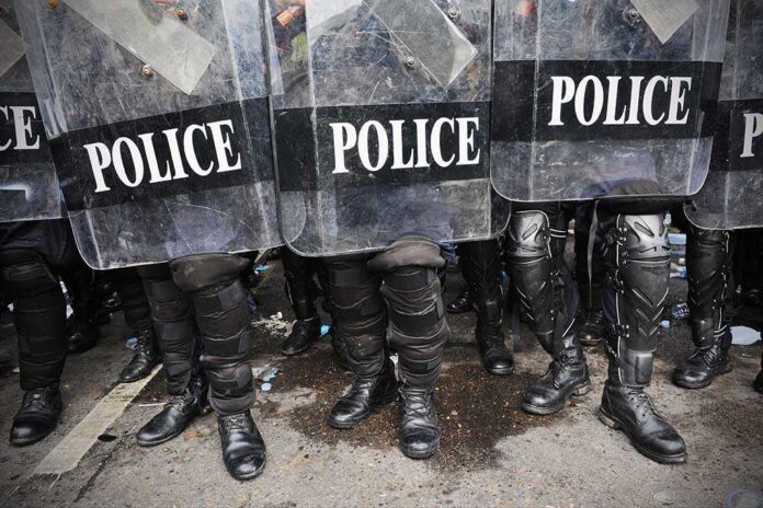 Police officers in riot gear standing behind shields marked POLICE