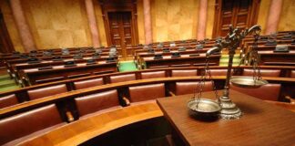 A courtroom with empty seats and a scale of justice in the foreground