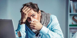 Man with tissue feeling unwell at laptop desk