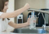 Girl filling glass with water from kitchen faucet.