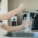 Cancer Risk SKYROCKETS—Tainted Tap Water Exposed Girl filling glass with water from kitchen faucet.