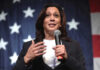 Woman speaking with microphone, American flag background.