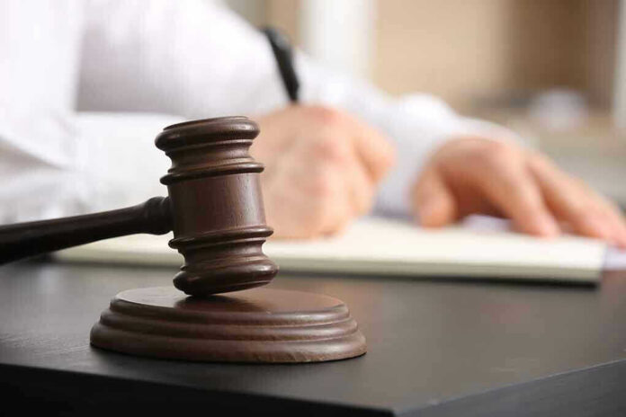 Judges gavel on desk with person writing.