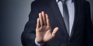 Man in suit with hand raised, signaling stop.