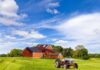 American Farmers BURIED by Brazil, Weather, and Debt A vintage tractor in front of a red barn on a sunny day