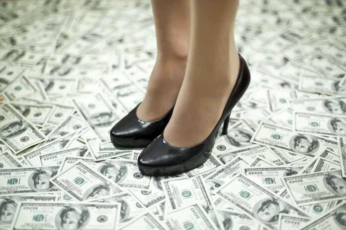 shutterstock_203119678.jpg A pair of black high heels standing on a floor covered with dollar bills