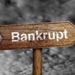 Founder’s Wild Spending Bombshell—ICON Company Collapses Wooden arrow sign pointing towards the word Bankrupt against a cloudy background