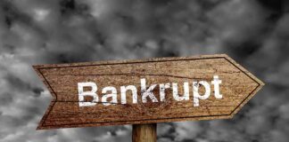Wooden arrow sign pointing towards the word Bankrupt against a cloudy background