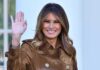 Melania Trump waving and smiling while wearing a stylish coat