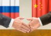 Two hands shaking in front of Russian and Chinese flags