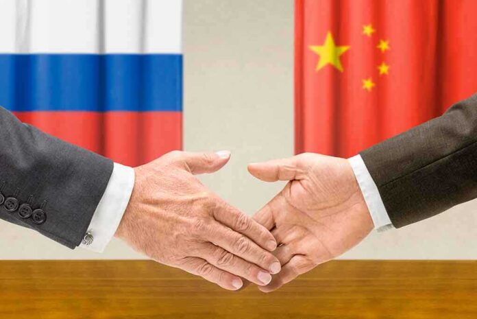 Two hands shaking in front of Russian and Chinese flags