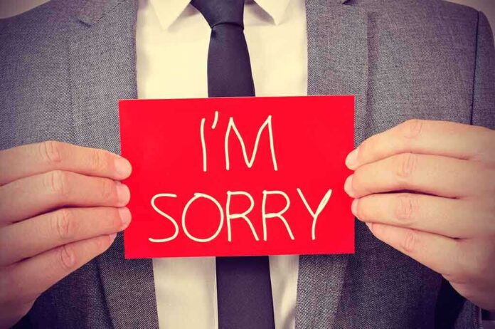 A person in a suit holding a red sign that says I'M SORRY
