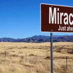 A road sign reading Miracles Just ahead in a desert landscape
