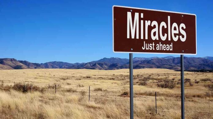 A road sign reading Miracles Just ahead in a desert landscape