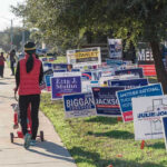 Kill Trump Video Rocks AG Race Person walking with stroller past numerous election campaign signs.