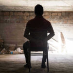Americans Held HOSTAGE: Charges MURKY Person tied to chair in dimly lit room.