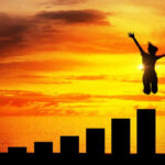 Silhouette jumping above bar chart at sunset.