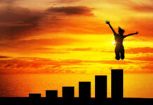 Silhouette jumping above bar chart at sunset.