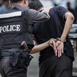 Police officer arrests handcuffed person.