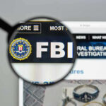 ESCALATION: Criminals Now Targeting Agent Families FBI website shown through magnifying glass.