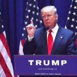 Tiny Nation Backs Trump’s Asylum Plan Donald Trump delivering a speech at a podium with American flags in the background
