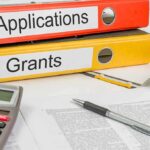 Two binders labeled Applications and Grants on a desk with a calculator and papers
