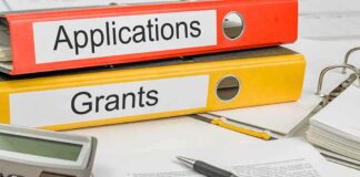 Two binders labeled Applications and Grants on a desk with a calculator and papers