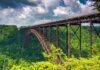 A large metal bridge spanning a lush green valley under a cloudy sky