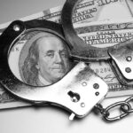 Handcuffs placed over a stack of hundred dollar bills