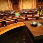 A courtroom with empty seats and a scale of justice in the foreground