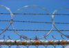 Barbed wire and metal fencing against blue sky.