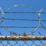 Barbed wire and metal fencing against blue sky.
