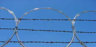 Barbed wire and metal fencing against blue sky.