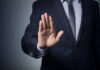 Man in suit with hand raised, signaling stop.
