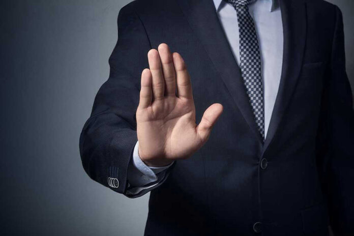 Man in suit with hand raised, signaling stop.