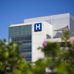DOJ Subpoenas Spark THESE Hospital Closures Modern hospital building with a prominent H sign against a clear blue sky