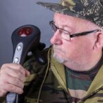 Elderly man in camouflage clothing holding a handheld device