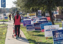 BIZARRE Candidate’s Claim: Toilets Are Now SOCIALISM Person walking with stroller past numerous election campaign signs.