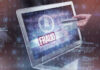 Person holding credit card near laptop displaying Fraud.