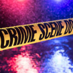 Yellow crime scene tape with police lights in background.