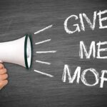 A hand holding a megaphone with the words GIVE ME MORE on a blackboard background