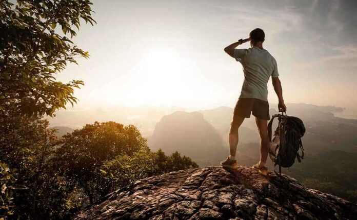 shutterstock_239978665.jpg Hiker standing on a rocky outcrop overlooking a valley at sunset