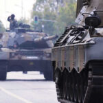 Tanks on a road with soldiers inside.