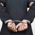 A person in a suit with hands cuffed behind their back