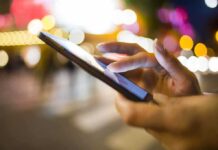 A persons hand using a smartphone in a city at night with blurred lights in the background