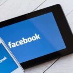 Smartphone and tablet displaying the Facebook logo on a wooden surface