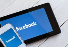 Smartphone and tablet displaying the Facebook logo on a wooden surface