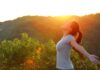 A woman standing outdoors with arms outstretched against a sunset backdrop