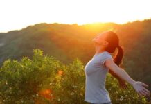 A woman standing outdoors with arms outstretched against a sunset backdrop